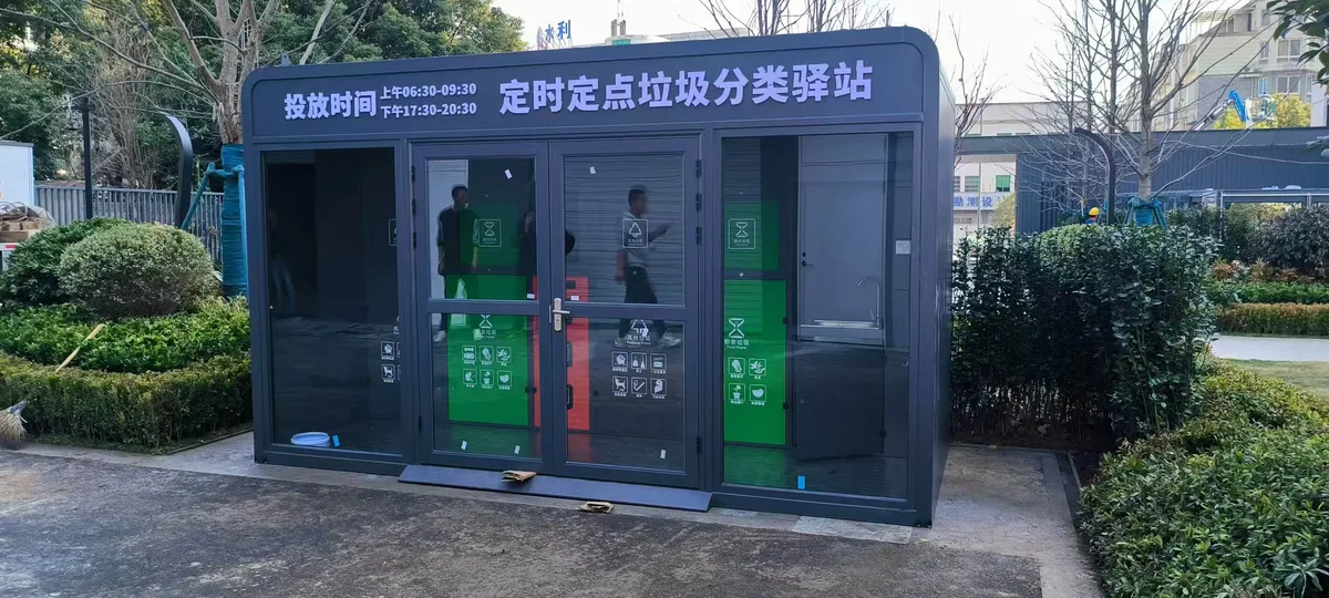 2024.02 华东某地区 SX-L 垃圾分类驿站案例:玻璃门与投放时间公示(图1) 户外深灰色定时定点垃圾分类驿站,前侧设玻璃门,入口上方公示两段投放时间